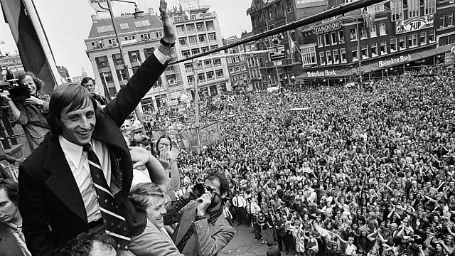 Cruyff saluant la foule à Amsterdam, en 1974. Par Nationaal Archief — Huldiging op Leidseplein in Amsterdam ; Cruyff wordt toegejuichdCollection / Archief : Fotocollectie AnefoNummer toegang : 2.24.01.05Filenumber : 927-3143, CC BY-SA 3.0 nl