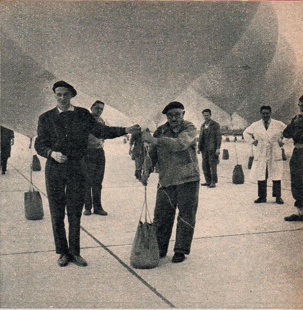 "Audouin Dollfuss (à gauche) procède aux derniers préparatifs de l'expédition sans précédent qui va l'entraîner jusque dans la stratosphère. Chaque ballon, une fois gonflé, est retenu ou sol, jusqu'à l'heure du départ, à l'aide d'un sac de sable. Les ballons seront ensuite tous réunis."