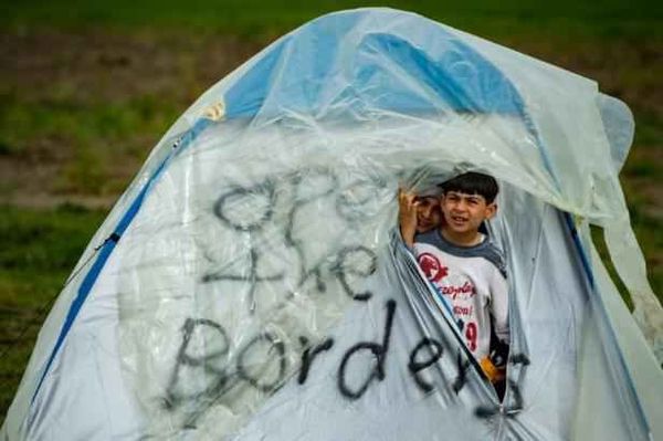 Du knaboj en tendo, sur kiu estas skribite « Malfermu la landlimojn », en migradkampejo ĉe la greka-makedonia landlimo en la vilaĝo Idomeno la 24an de marto 2016. - ANDREJ ISAKOVIC AFP