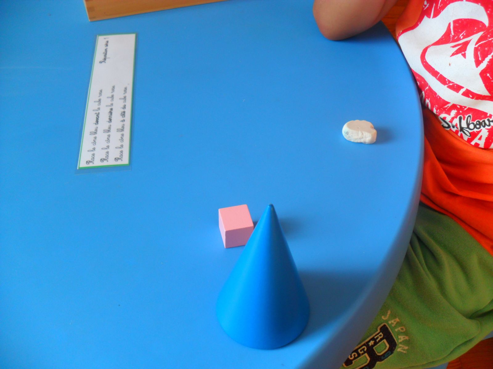 "Place le cône bleu à côté du cube rose"
