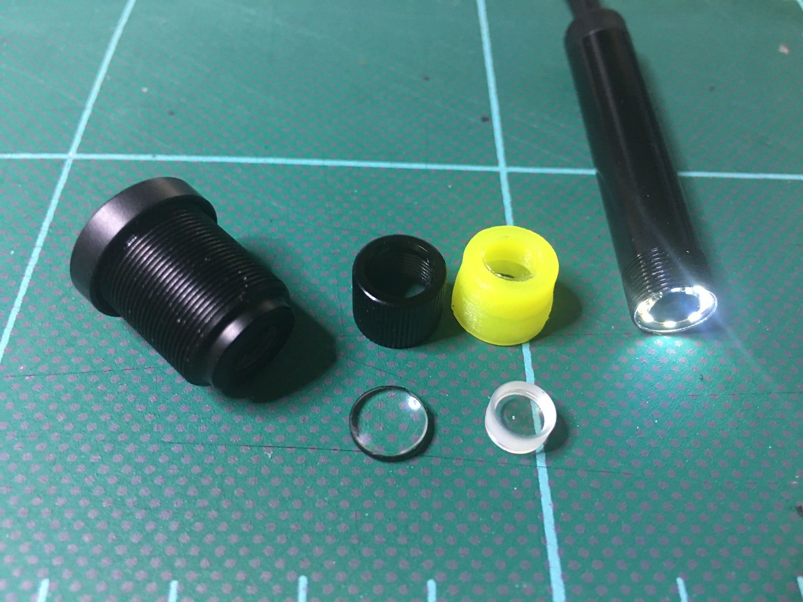 Dans l'ordre de gauche à droite, une lentille complete de Webcam PC : contient plusieures lentilles convexes et concaves, la lentille convexe et embout noir, la lentille concave et embout jaune, la tête d'endoscope