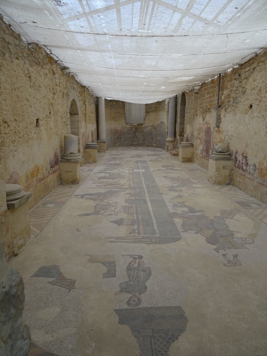 Le gymnase, grande salle avec deux absides aux extrémités, où l'on se réchauffait les muscles avant les bains. Le décor représente les quadriges s'affrontant au cirque Maximus de Rome.