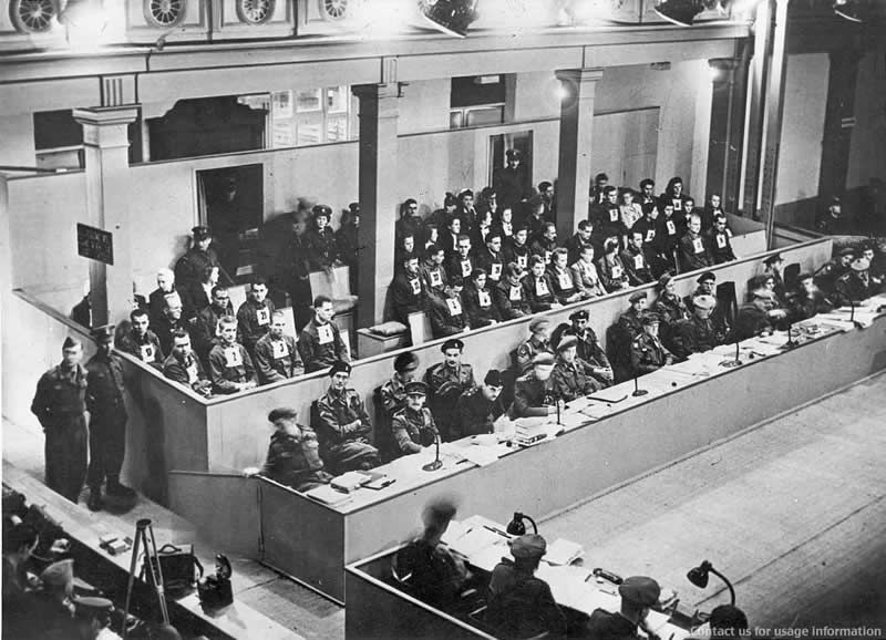 Le procès de Bergen-Belsen se tient à Lüneburg du 17 septembre au 17 novembre 1945. Les SS sont jugés par un tribunal militaire britannique. Les accusés, hommes et femmes, sont pourvus de numéros accrochés sur leur poirtine. Au premier rang à gauche, portant le numéro 1, figure Josef Kramer, dernier commandant du camp de Bergen-Belsen. Photographie du banc des accusés, automne 1945