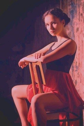 Une belle et jeune femme écarte les jambes, chevauche une chaise. Il y a un homme assis devant une page encore vierge.