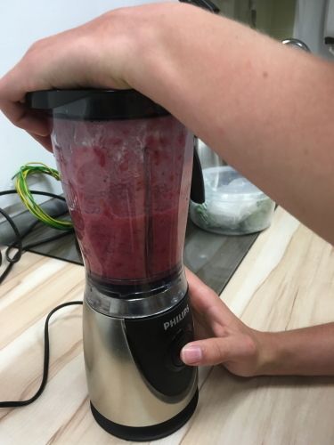 Roter Johannisbeersaft in einem Mixer. En Schüler drückt den Knopf des Mixers und hält ihn fest.
