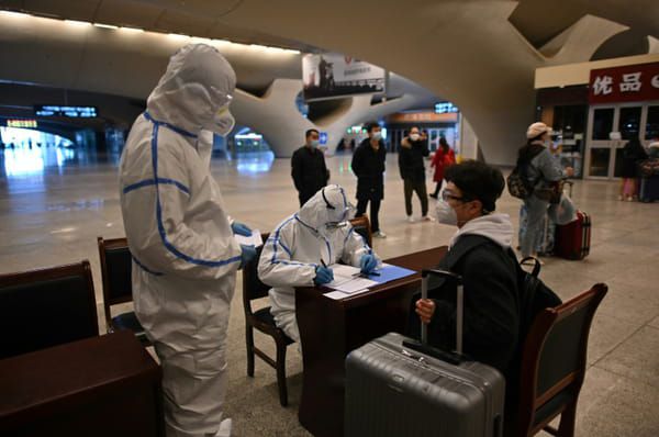 Un employé en combinaison de protection vérifie les documents d'identité des voyageurs arrivant à la gare de Wuhan, dans la province chinoise du Hubei, le 28 mars 2020 © AFP - HECTOR RETAMAL