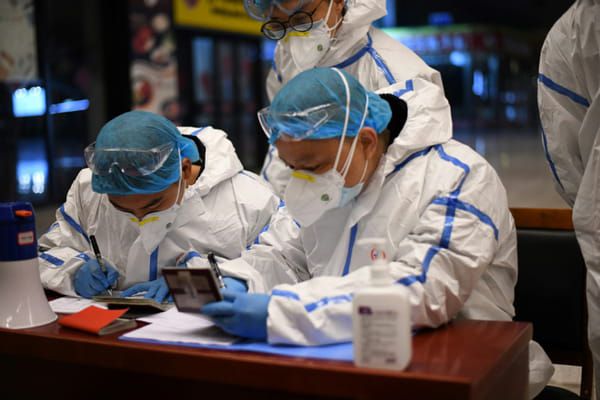 Des employés en combinaison de protection contrôleent les documents d'identité des voyageurs arrivant à la gare de Wuhan, dans la province chinoise du Hubei, le 28 mars 2020 © AFP - Noel Celis