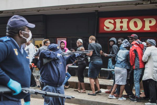 Un policier sud-africain pointe son fusil à balles en caoutchouc sur la foule pour faire respecter les consignes de distance sociale devant un supermarché de Johannesburg, le 28 mars 2020, pendant le confinement instauré pour lutter contre l'épidémie du nouveau coronavirus © AFP - MARCO LONGARI